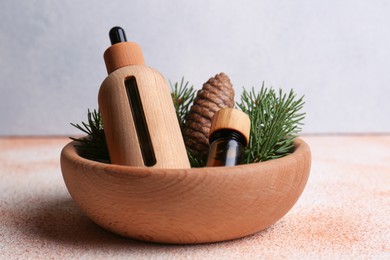 Photo of Bowl with bottles of aromatic essential oil, pine branches and cone on color table, closeup