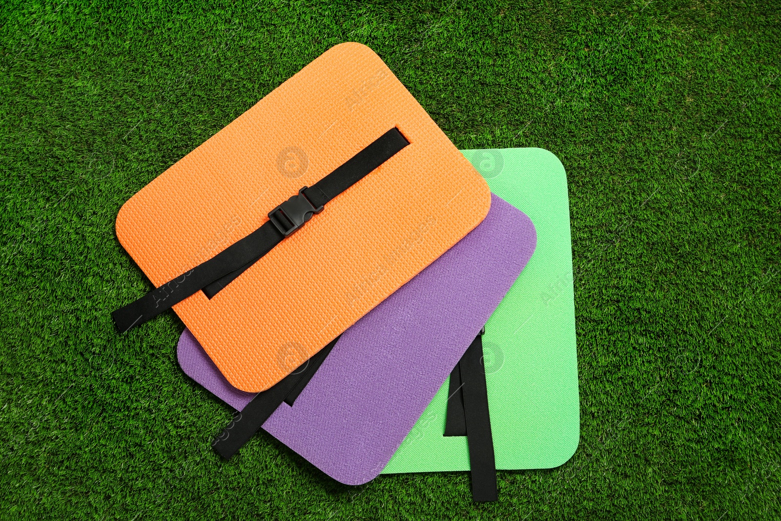 Photo of Bright foam tourist seat mats on green grass, flat lay