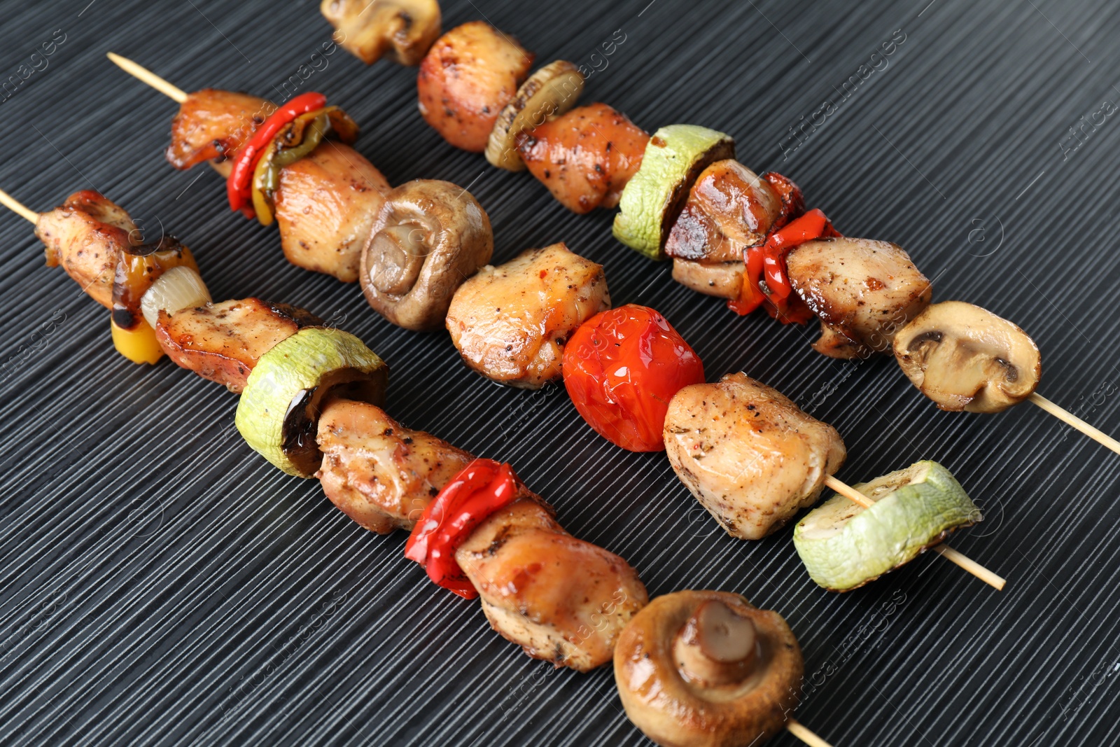 Photo of Delicious shish kebabs with vegetables on black table, closeup