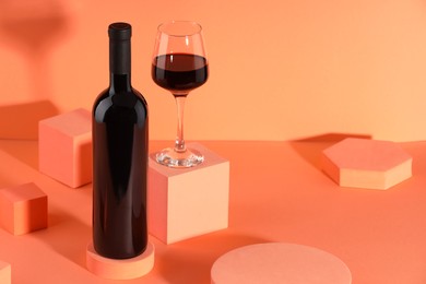 Stylish presentation of delicious red wine in bottle and glass on orange background