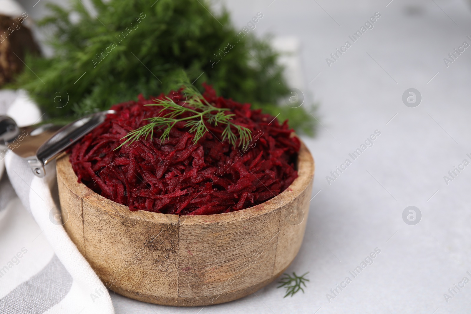 Photo of Grated red beet and dill in wooden bowl on light gray table, closeup. Space for text