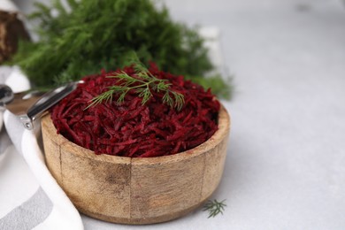 Photo of Grated red beet and dill in wooden bowl on light gray table, closeup. Space for text