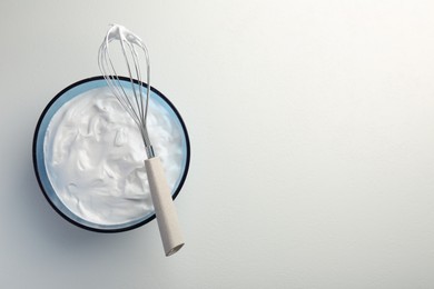 Photo of Bowl with whipped cream and whisk on light background, top view. Space for text
