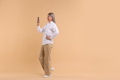 Photo of Senior woman with phone on beige background, space for text