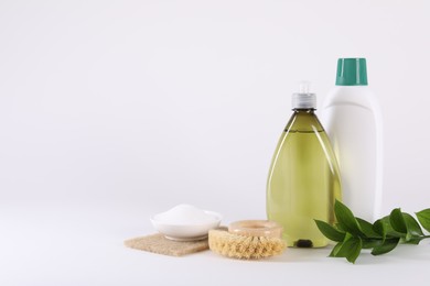 Bottles of cleaning product, brush, baking soda and green leaves on white background