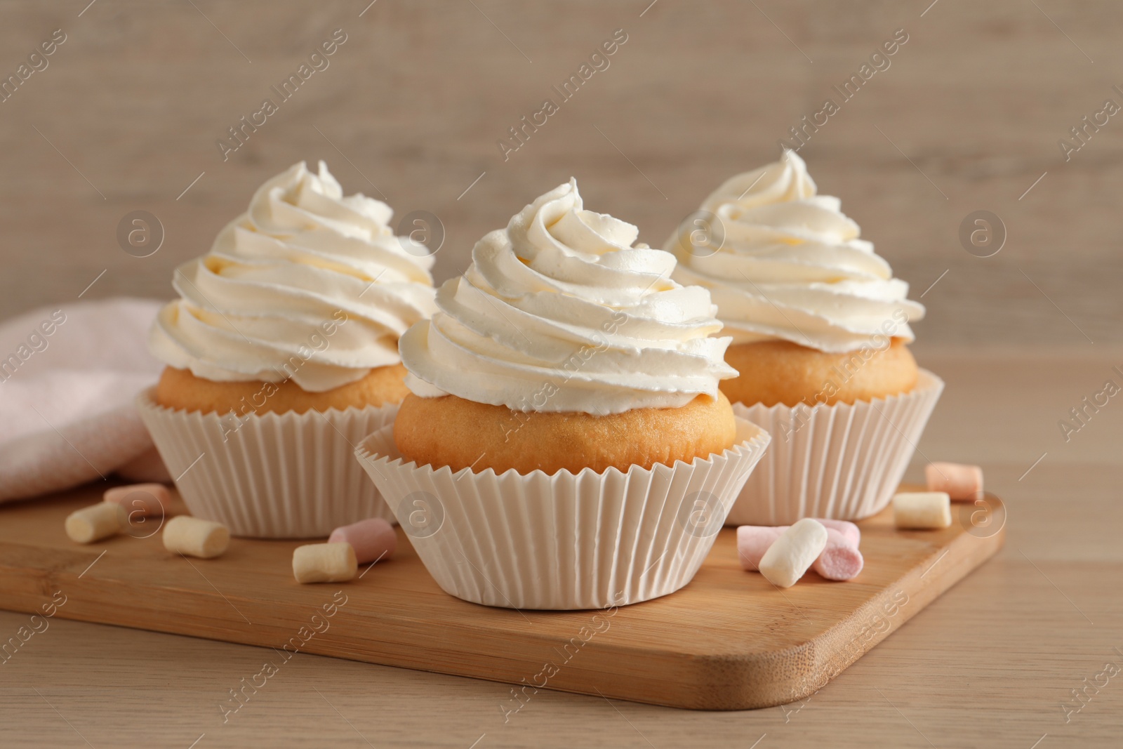 Photo of Delicious cupcakes with cream and marshmallows on wooden table