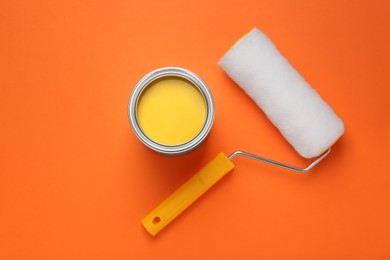 Photo of Can with yellow paint and roller on orange background, flat lay