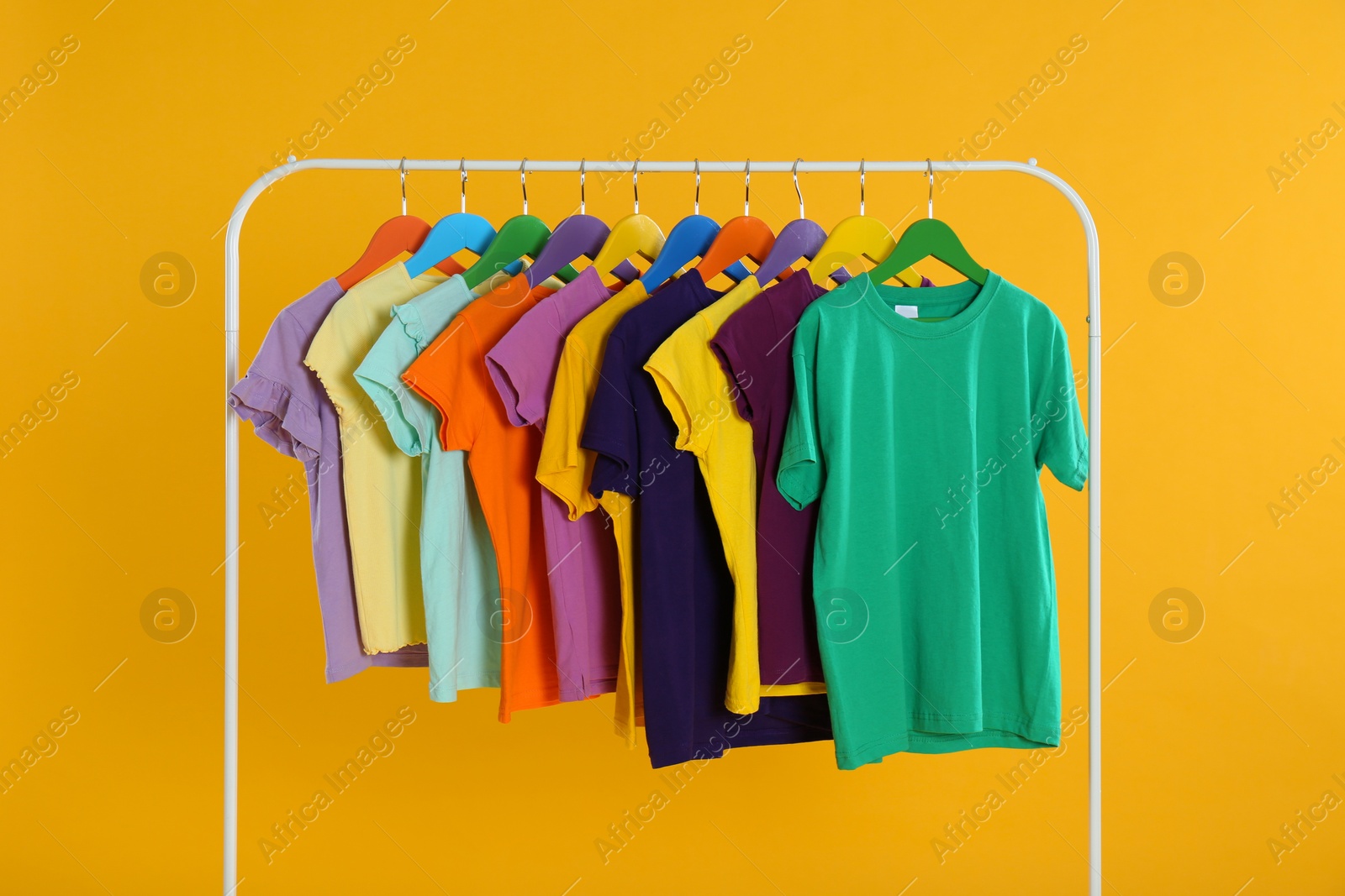 Photo of Rack with stylish children clothes on yellow background