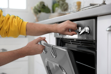 Photo of Man using modern oven in kitchen, closeup
