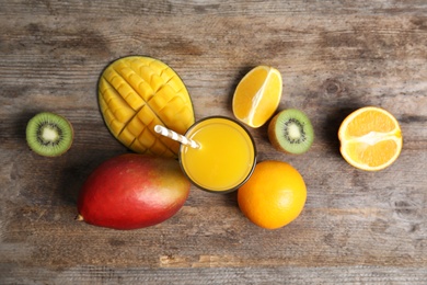 Glass with fresh mango juice and tasty fruits on wooden table, flat lay