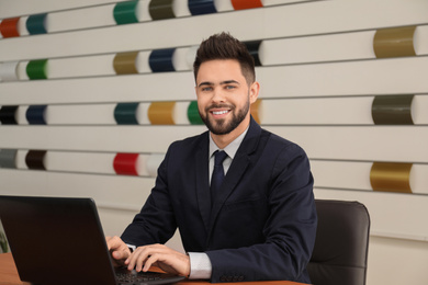 Photo of Salesman working with laptop at desk in car dealership