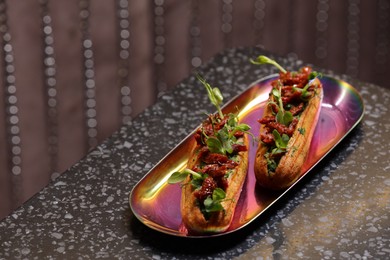 Photo of Tasty eclairs with sun-dried tomatoes and microgreens on dark table. Space for text