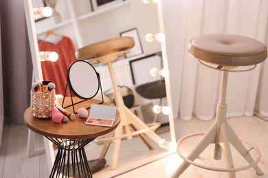 Photo of Makeup room. Stylish mirror with light bulbs, beauty products on wooden table and chair indoors
