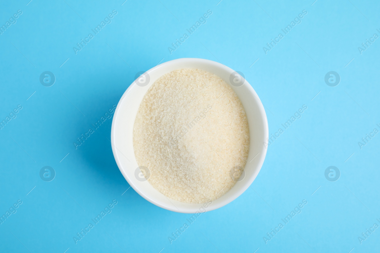 Photo of Gelatin powder in bowl on light blue background, top view