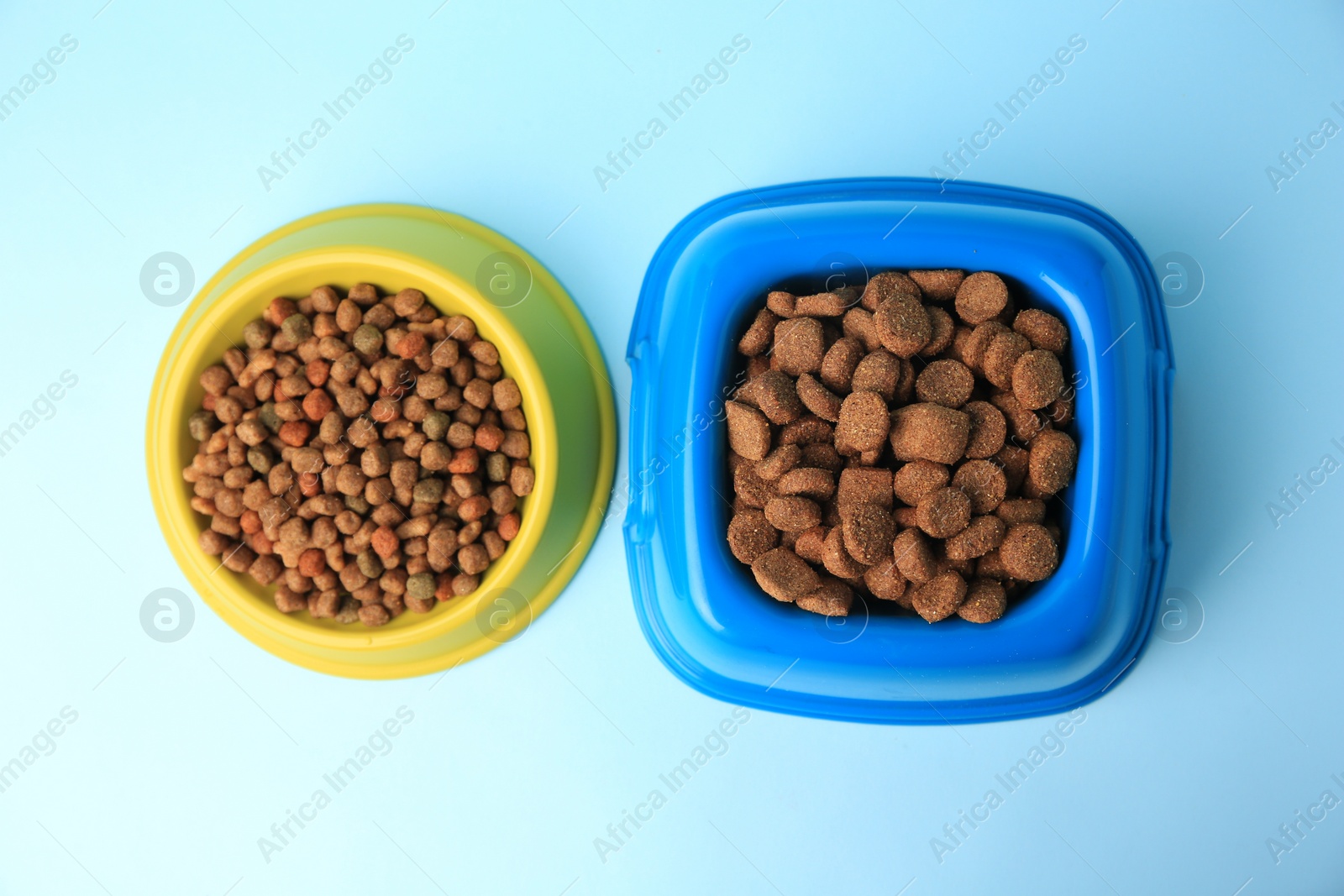 Photo of Dry pet food in feeding bowls on light blue background, flat lay