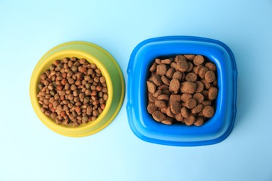 Dry pet food in feeding bowls on light blue background, flat lay