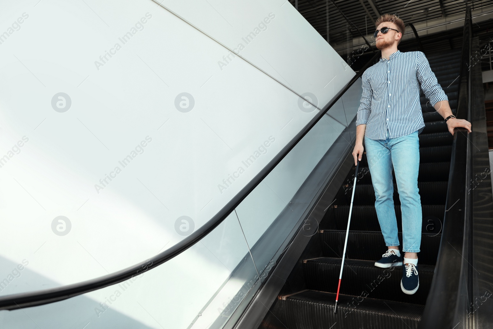 Photo of Blind person with long cane on escalator indoors. Space for text