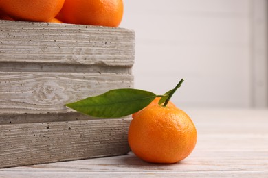 Photo of Delicious tangerine with leaf and crate on light wooden table, closeup. Space for text