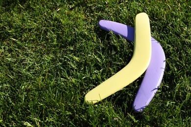 Photo of Violet and yellow wooden boomerangs on green grass outdoors, space for text