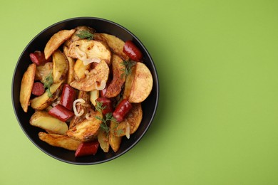 Photo of Delicious baked potato with thin dry smoked sausages, onion and dill in bowl on green table, top view. Space for text