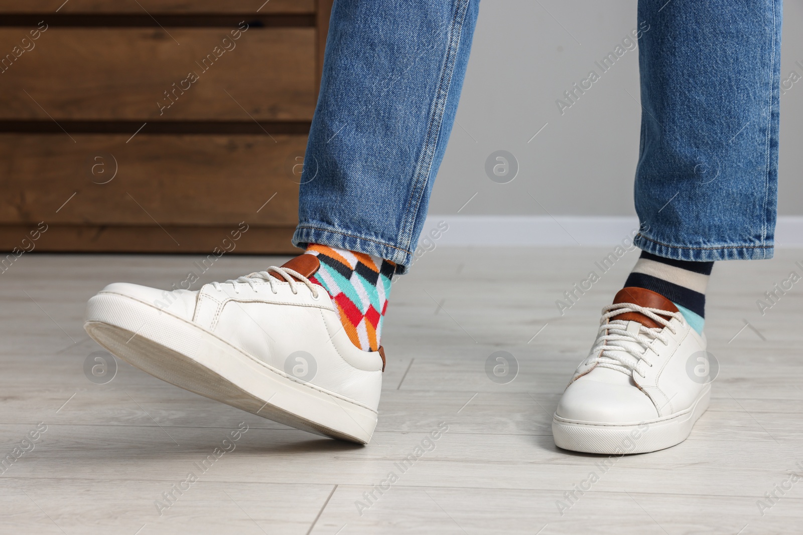 Photo of Man in different stylish socks, sneakers and jeans indoors, closeup