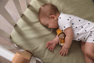Photo of Adorable little baby with pacifier and toy sleeping in crib, above view
