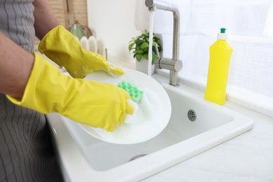 Man washing plate above sink in kitchen, closeup