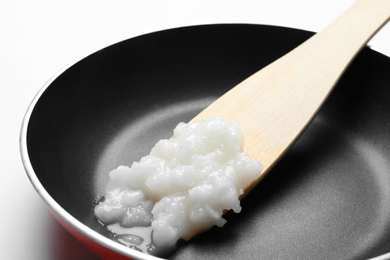 Frying pan with coconut oil and wooden spatula on white background, closeup. Healthy cooking