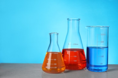Glass flasks with colorful liquids on wooden table against light blue background. Space for text