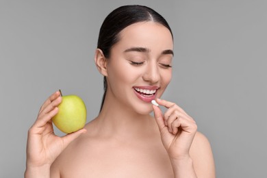 Photo of Beautiful young woman with vitamin pill and apple on grey background