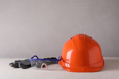 Photo of Hard hat, goggles and gloves on white table, space for text. Safety equipment