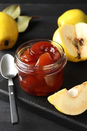 Quince jam in glass jar, spoon and fresh raw fruits on grey table