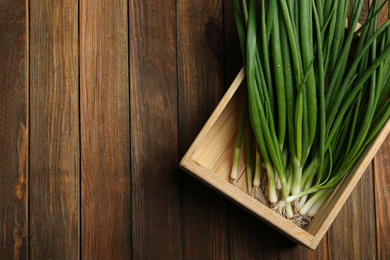 Photo of Fresh green spring onions in crate on wooden table, top view. Space for text