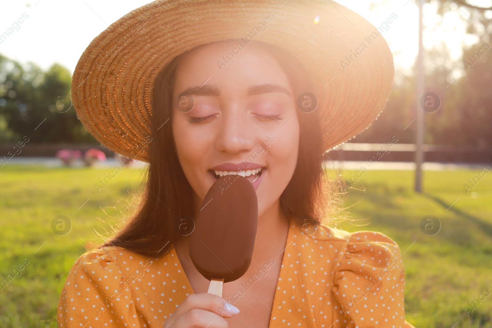 Photo of Beautiful young woman eating ice cream glazed in chocolate outdoors, closeup