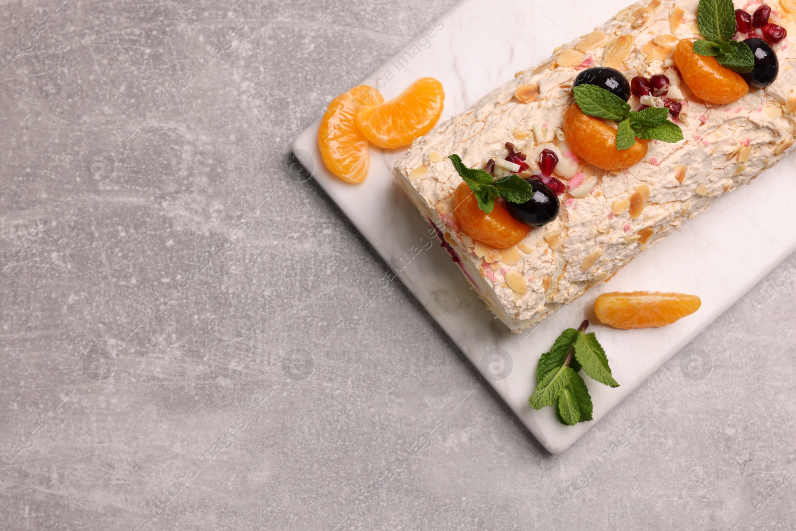 Photo of Tasty meringue roll with tangerine slices and mint leaves on grey table, top view. Space for text