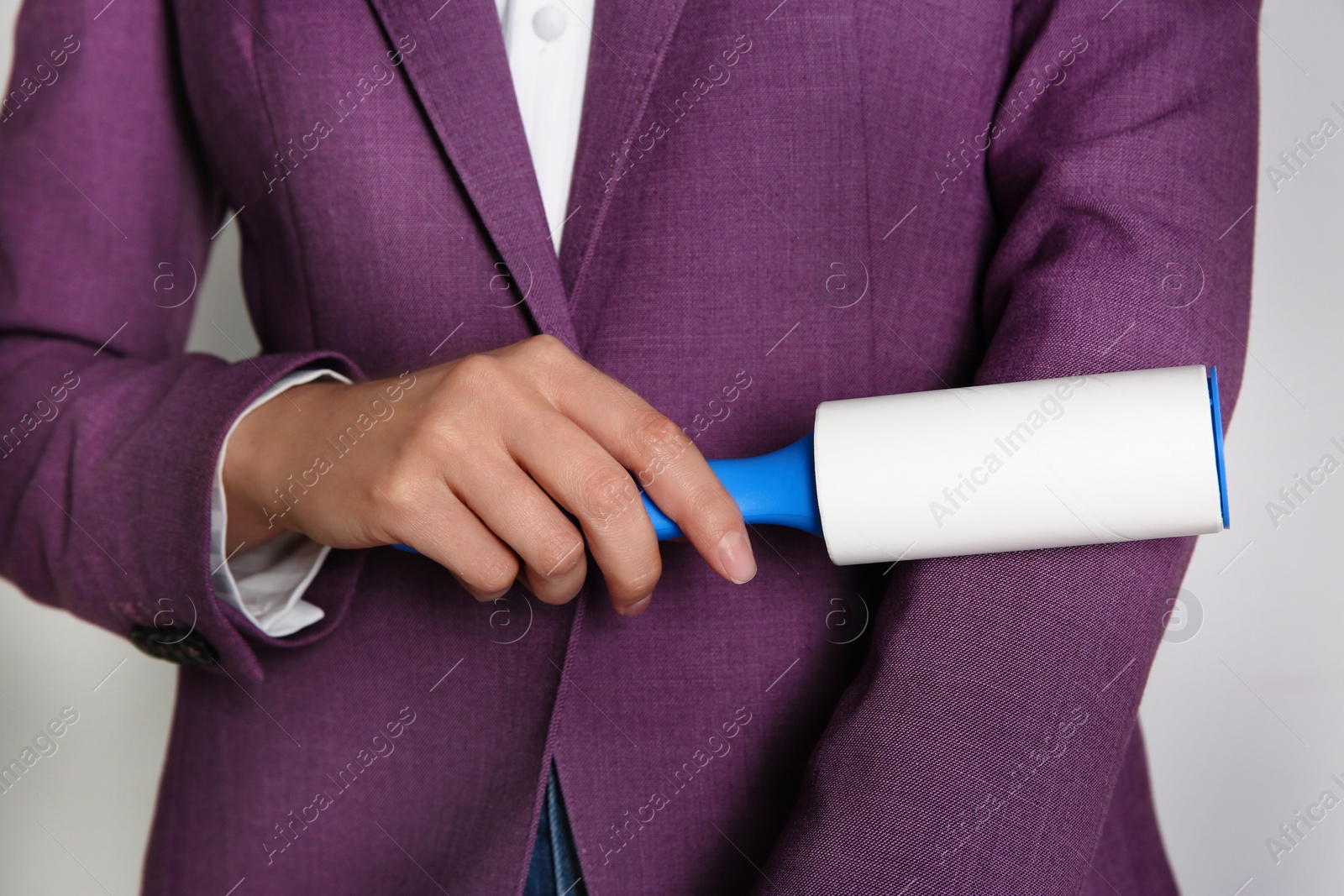 Photo of Woman cleaning purple jacket with lint roller on light grey background, closeup