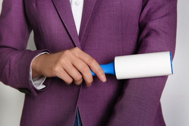 Woman cleaning purple jacket with lint roller on light grey background, closeup