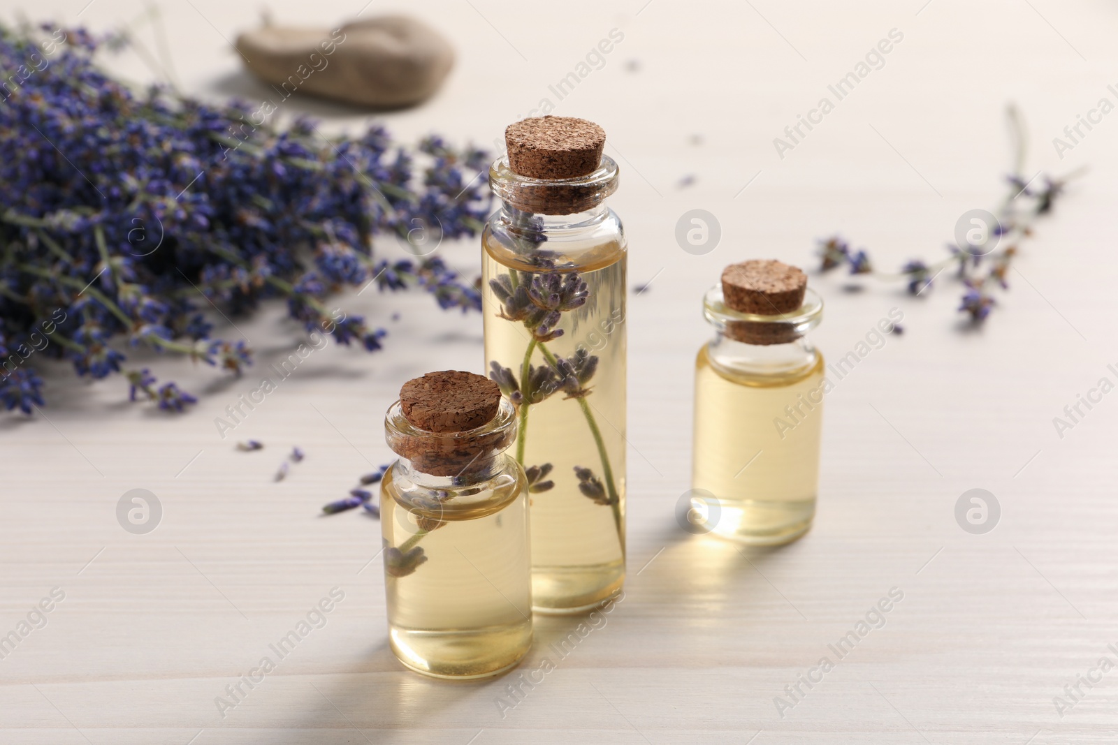 Photo of Essential oil and lavender flowers on white wooden table