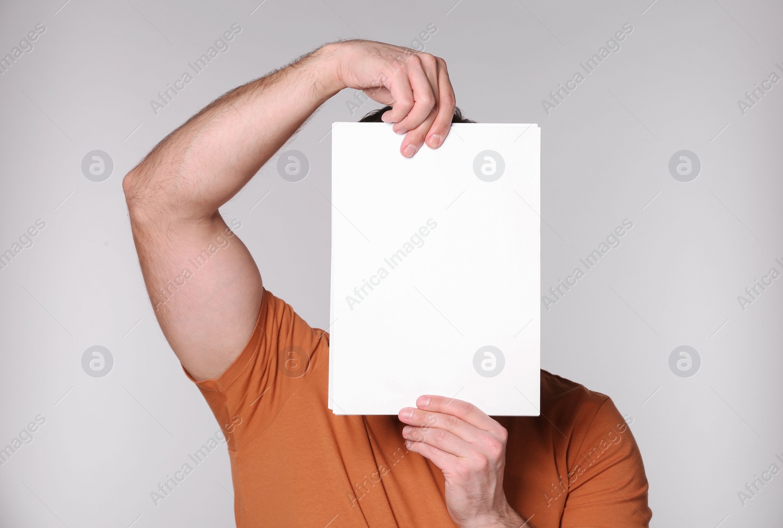 Photo of Man covering face with sheet of paper on light grey background. Mockup for design