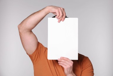 Man covering face with sheet of paper on light grey background. Mockup for design