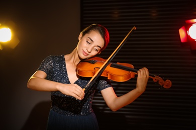 Photo of Beautiful young woman playing violin in dark room