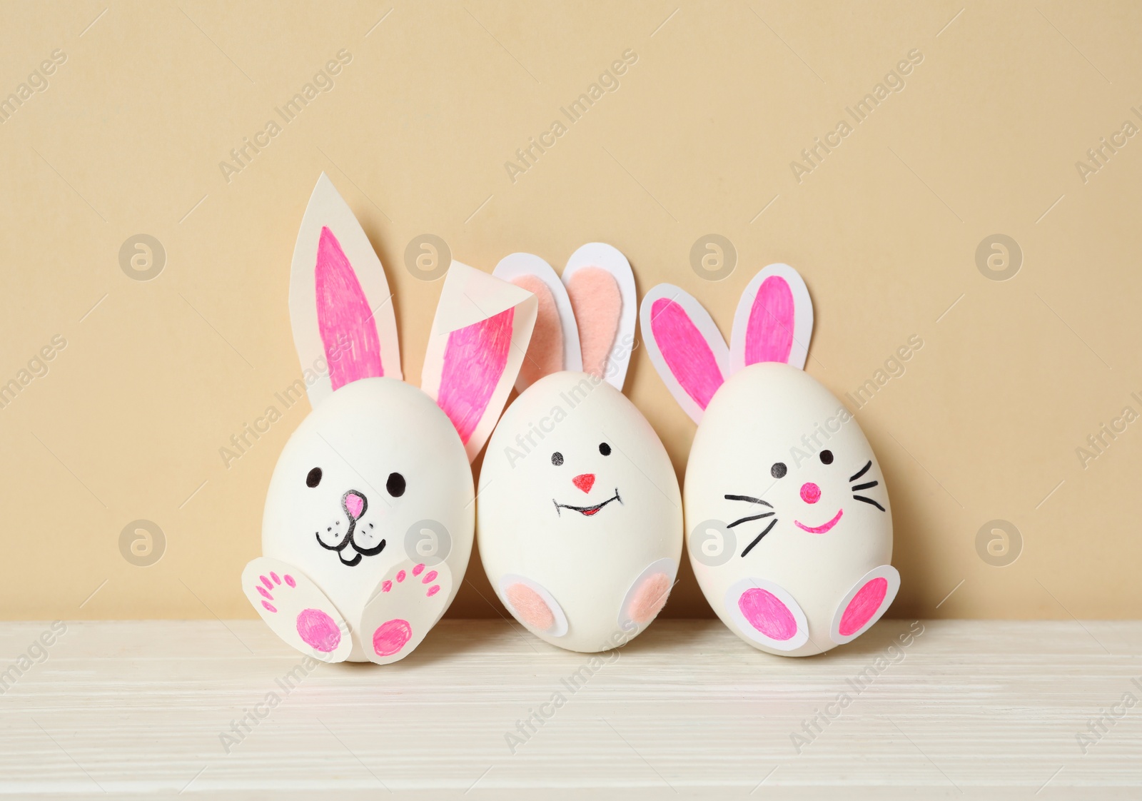 Photo of Eggs as cute bunnies on white wooden table against beige background. Easter celebration
