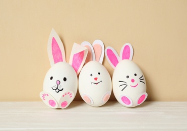 Eggs as cute bunnies on white wooden table against beige background. Easter celebration