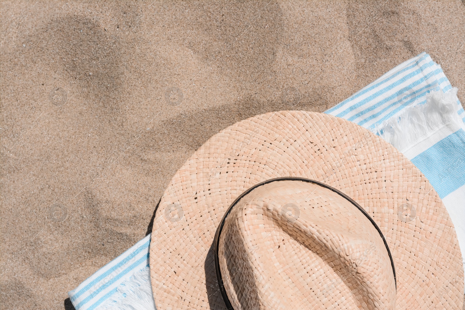 Photo of Straw hat and beach towel on sand, top view. Space for text