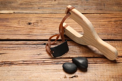 Photo of Slingshot with stones on wooden table. Space for text