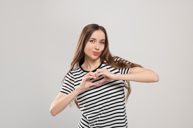 Photo of Beautiful young woman blowing kiss and making heart with hands on light grey background