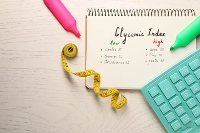 Photo of List with products of low and high glycemic index in notebook, markers, measuring tape and calculator on white wooden table, flat lay. Space for text