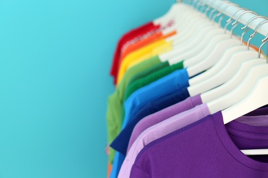 Rack with rainbow clothes on color background