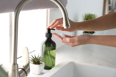 Photo of Woman using soap dispenser in kitchen, closeup