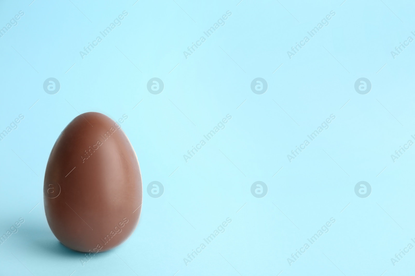 Photo of Sweet chocolate egg on light blue background. Space for text